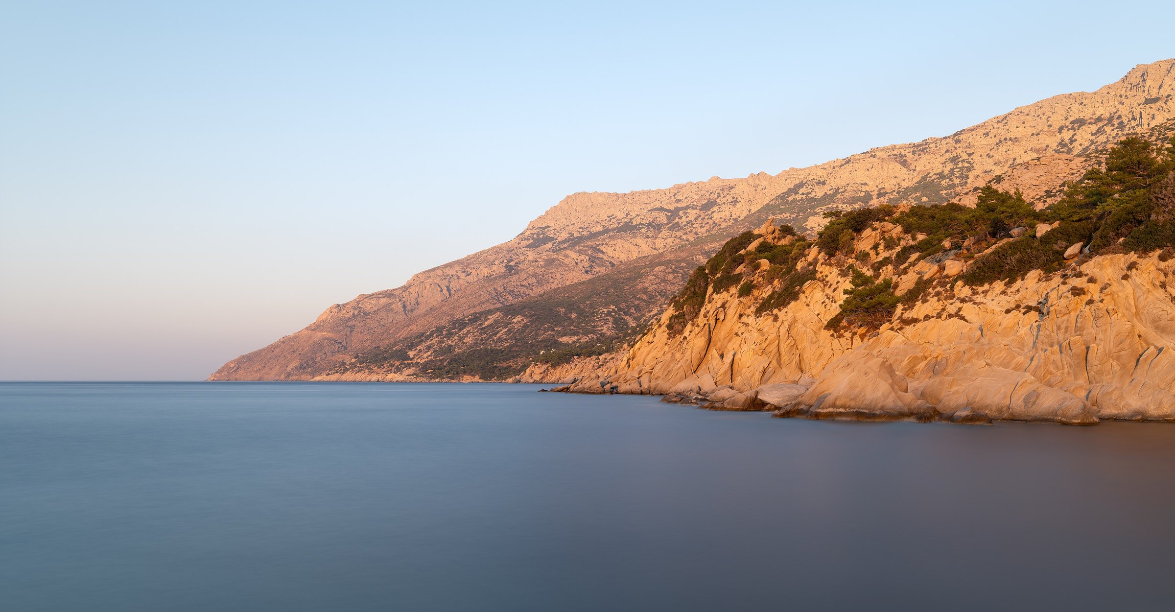 Dawn light over the cliffs and still water at the port of Manganitis, Ikaria, Greece